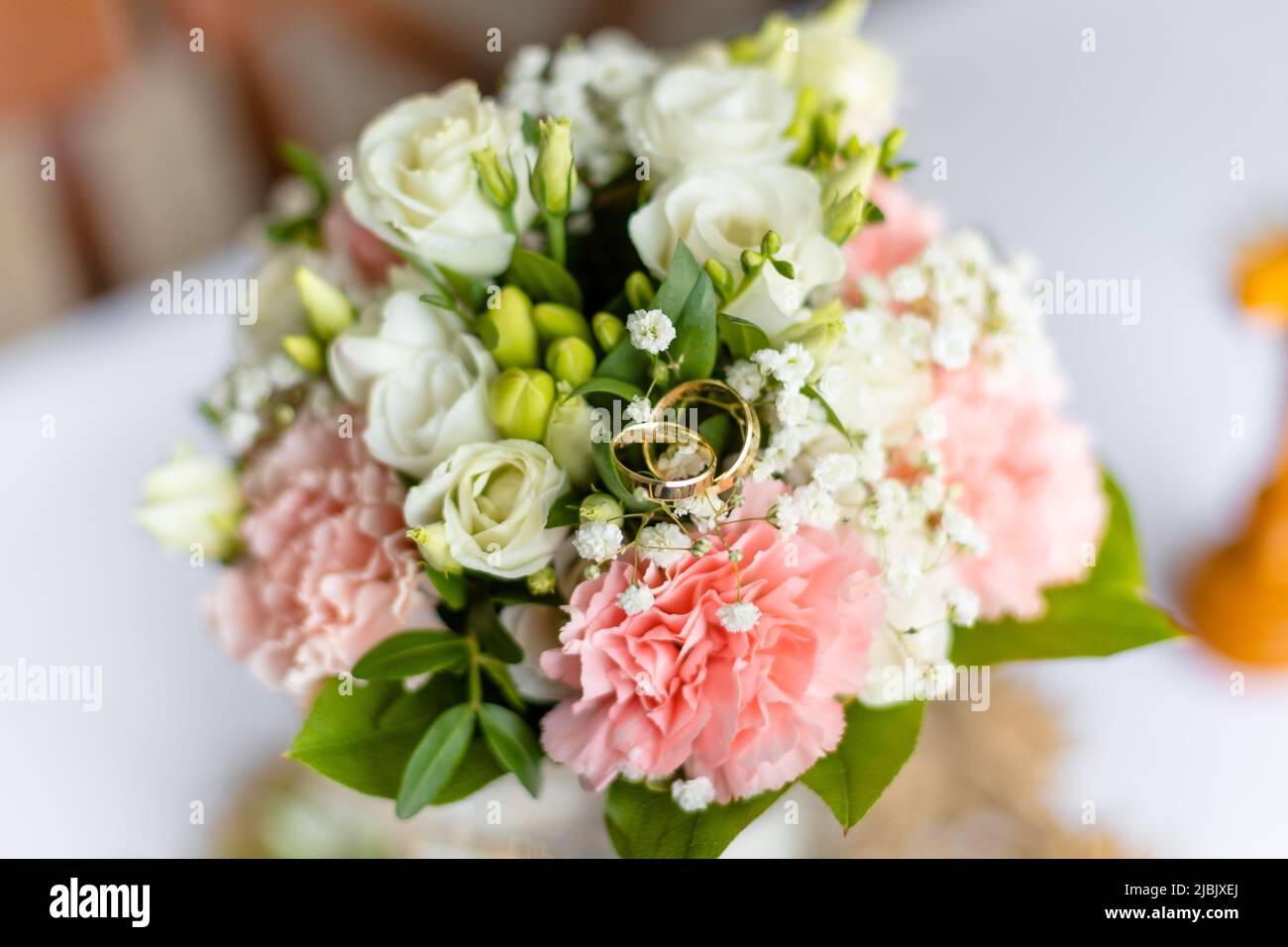 Soft bridal bouquet of fresh flowers and wedding gold rings on celebratory table closeup, blurred background. Elegant attribute and tradition Stock Photo
