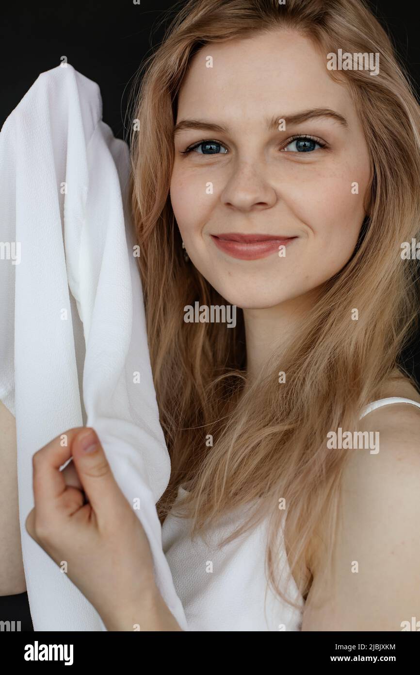 Portrait closeup of happy young attractive lady with blue eyes and perfect makeup holding white clothing on black background. Fashion studio shooting Stock Photo