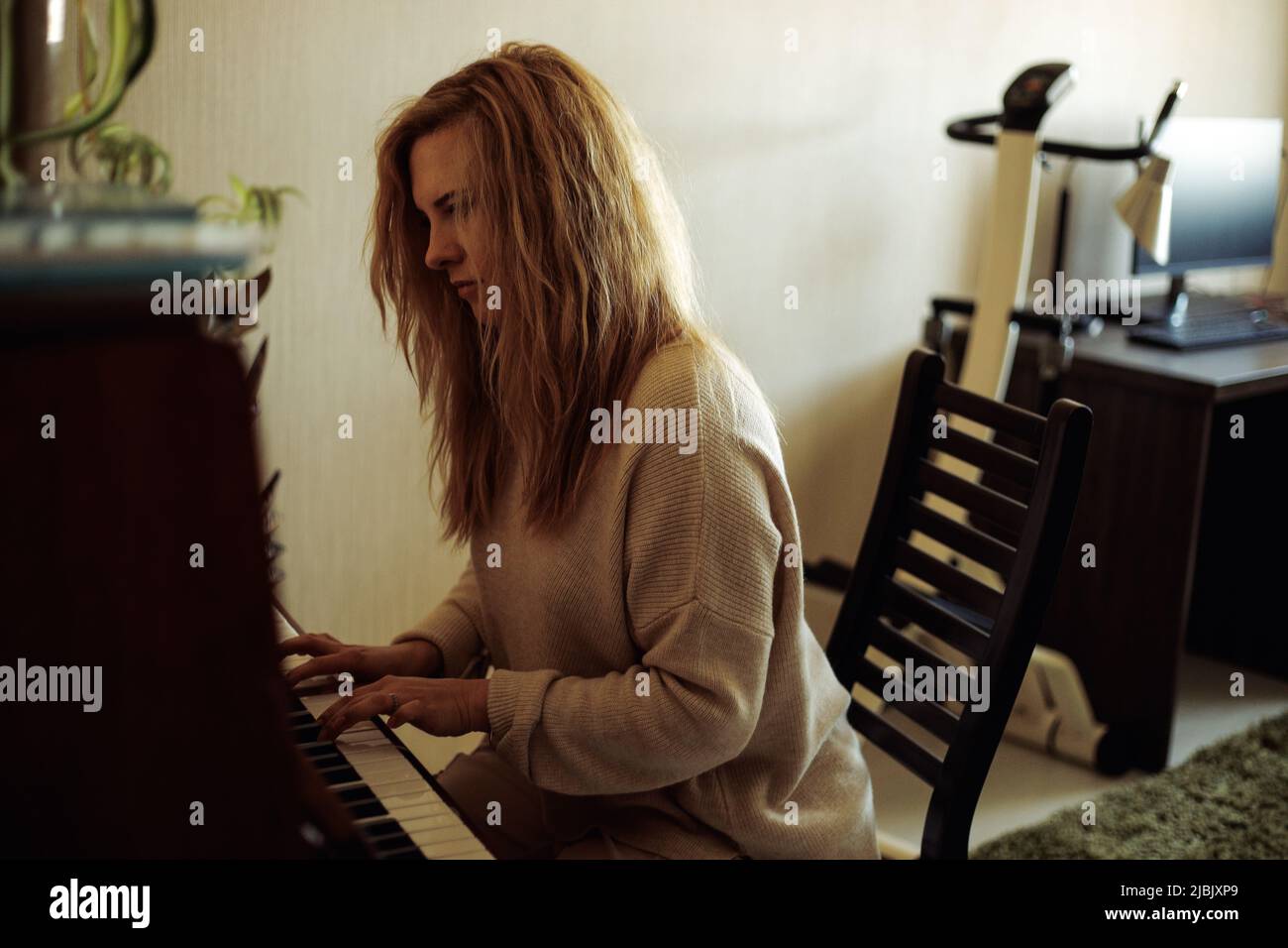 Beautiful blonde woman in home clothes sitting at piano, pressing keys ...