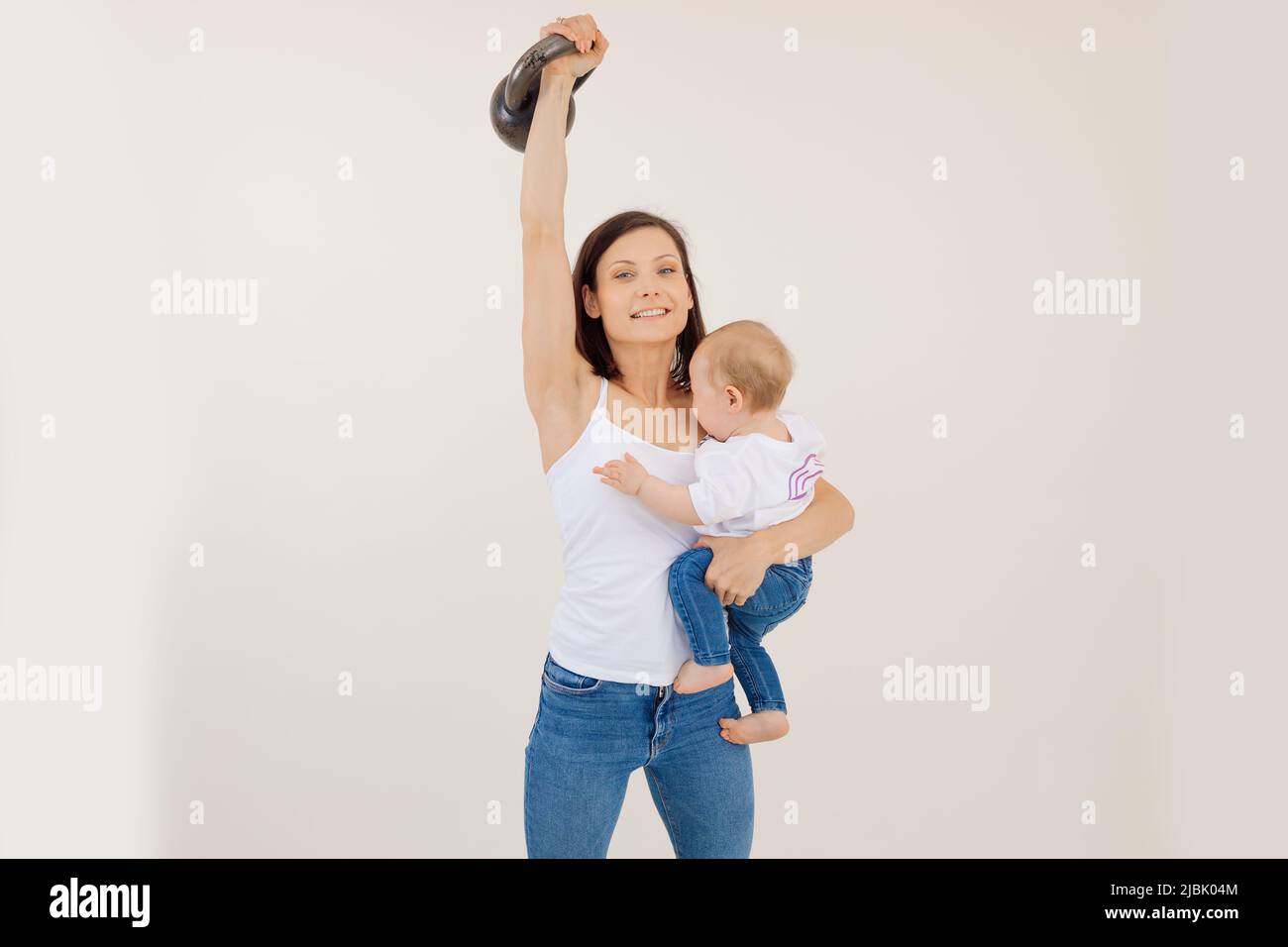 Young athletic smiling woman lifting up kettlebell and holding little ...