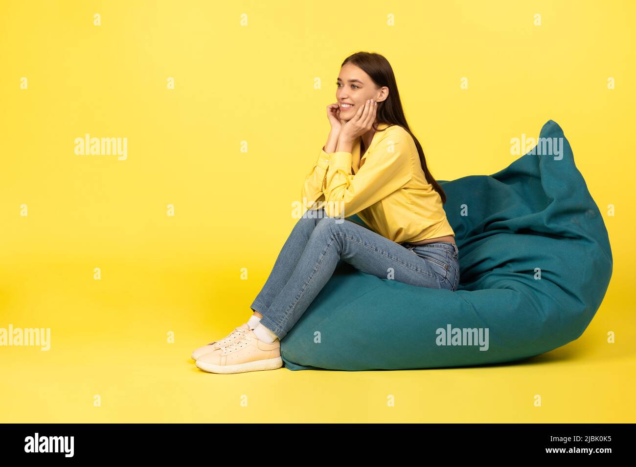 Woman Sitting In Bean Bag Chair Posing Over Yellow Background Stock Photo