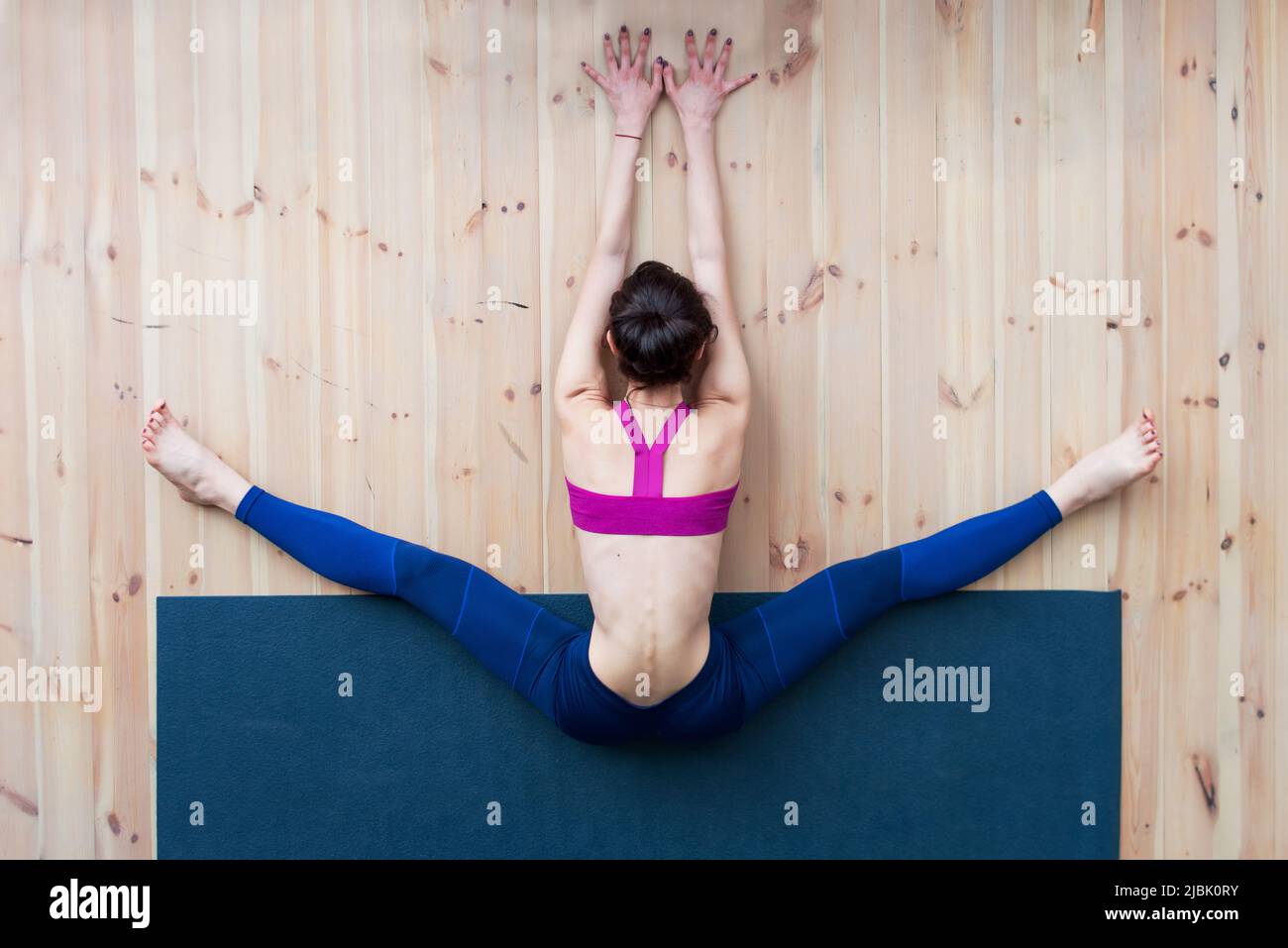 Young girl performing wide-angle seated forward bend or upavistha konasana during stretching class in gym. Stock Photo