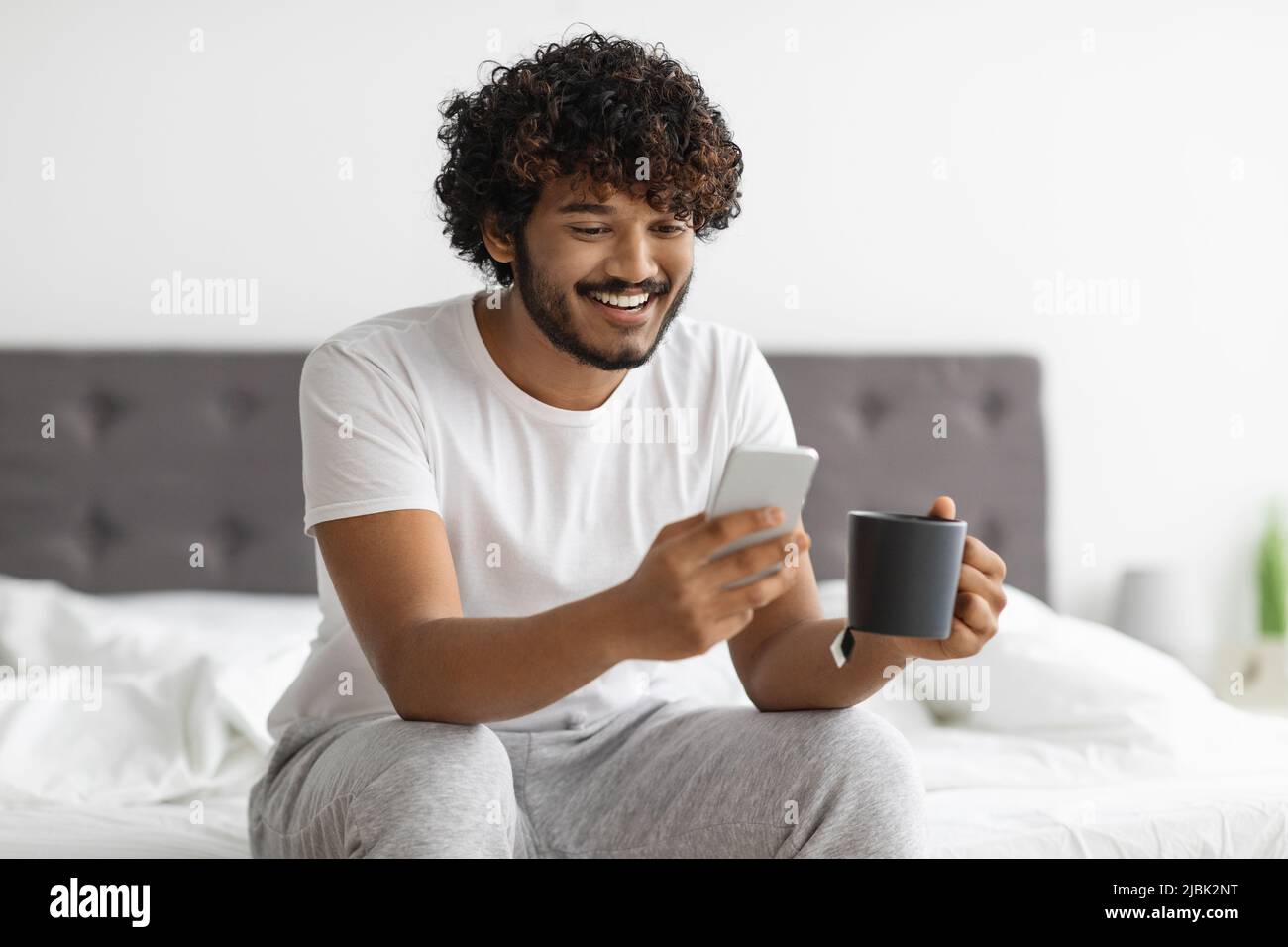 Cheerful eastern man drinking coffee and using smartphone Stock Photo