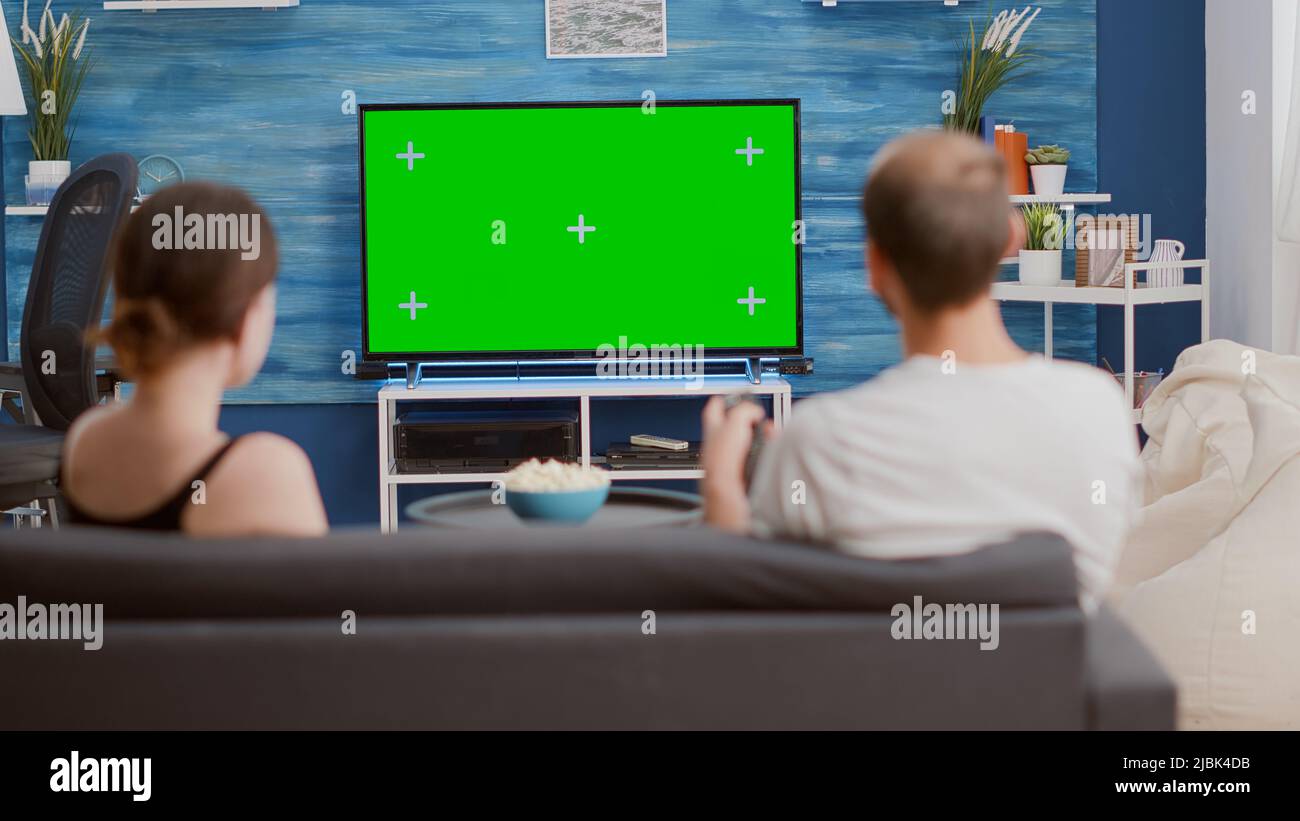 Back view of young woman asking boyfriend to change tv channel on green