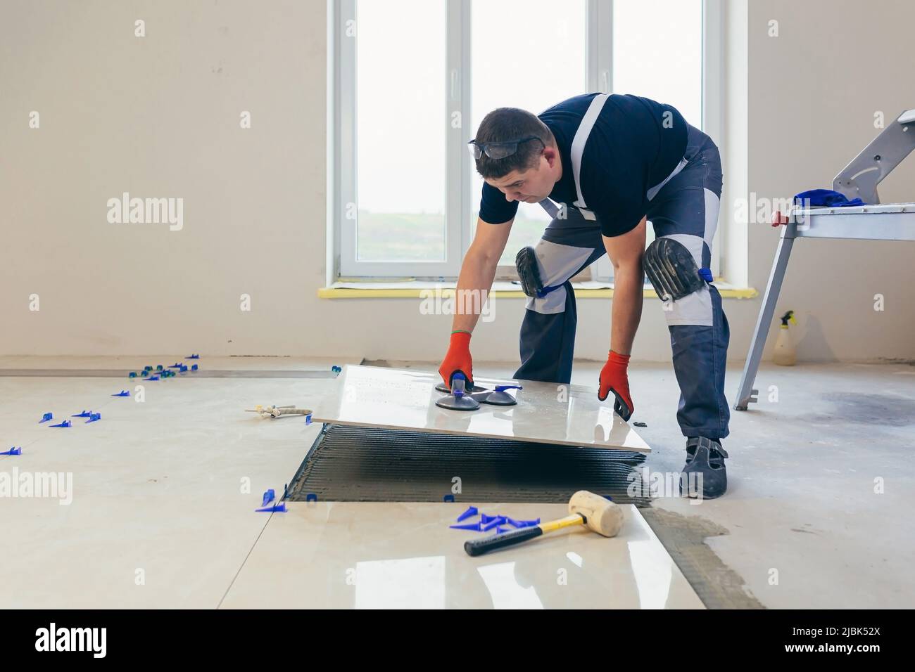 A male construction worker installs a large ceramic tile Stock Photo