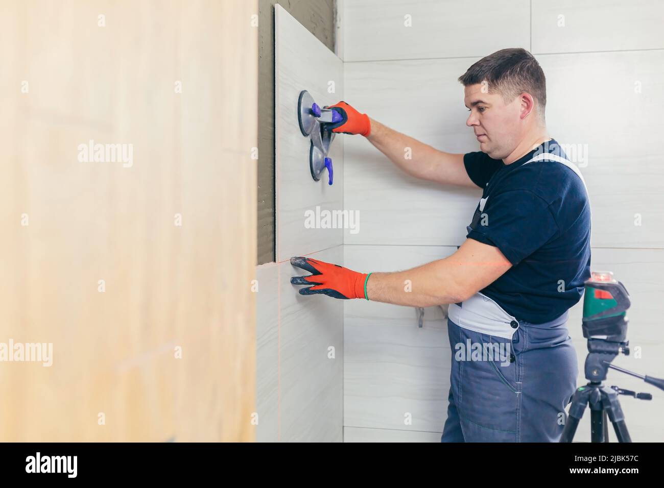 A male construction worker installs a large ceramic tile Stock Photo