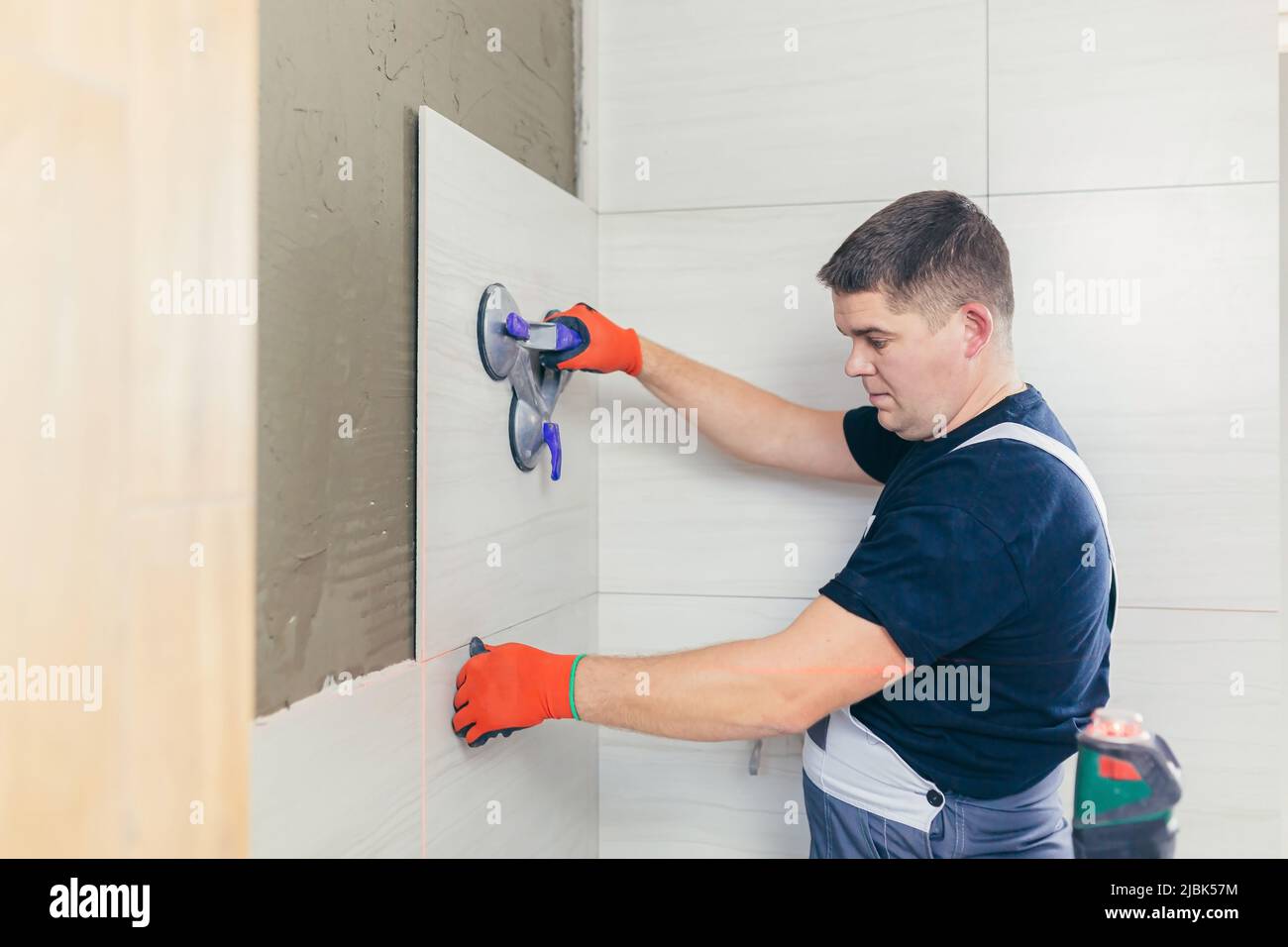 A male construction worker installs a large ceramic tile Stock Photo