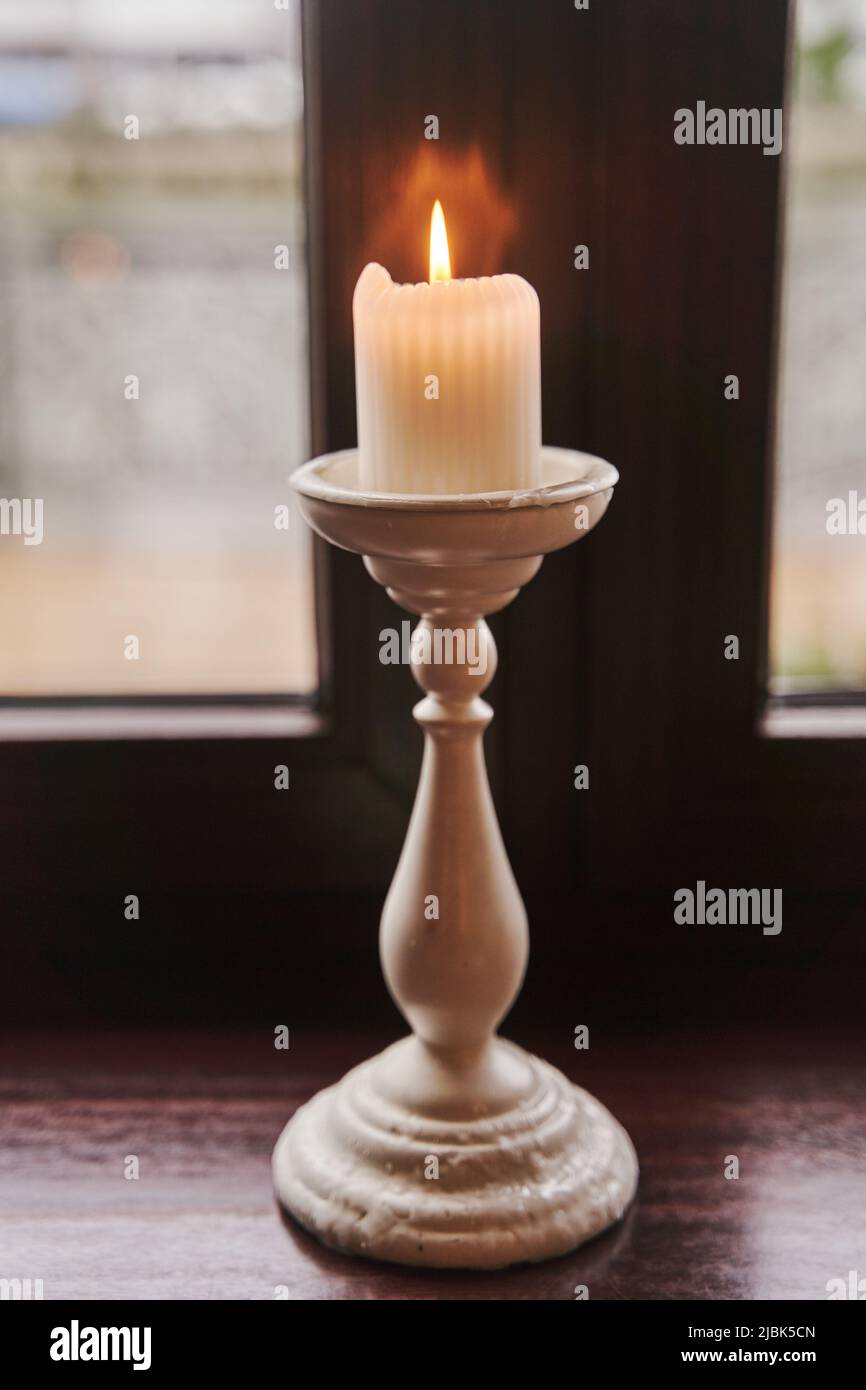 A burning candle in a candlestick stands on the windowsill Stock Photo