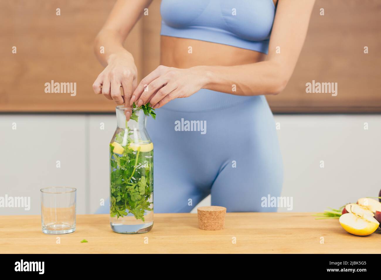 Close up photo, body part of young beautiful fitness woman preparing detox drink with fresh fruits, mint and lemon at home in the kitchen Stock Photo