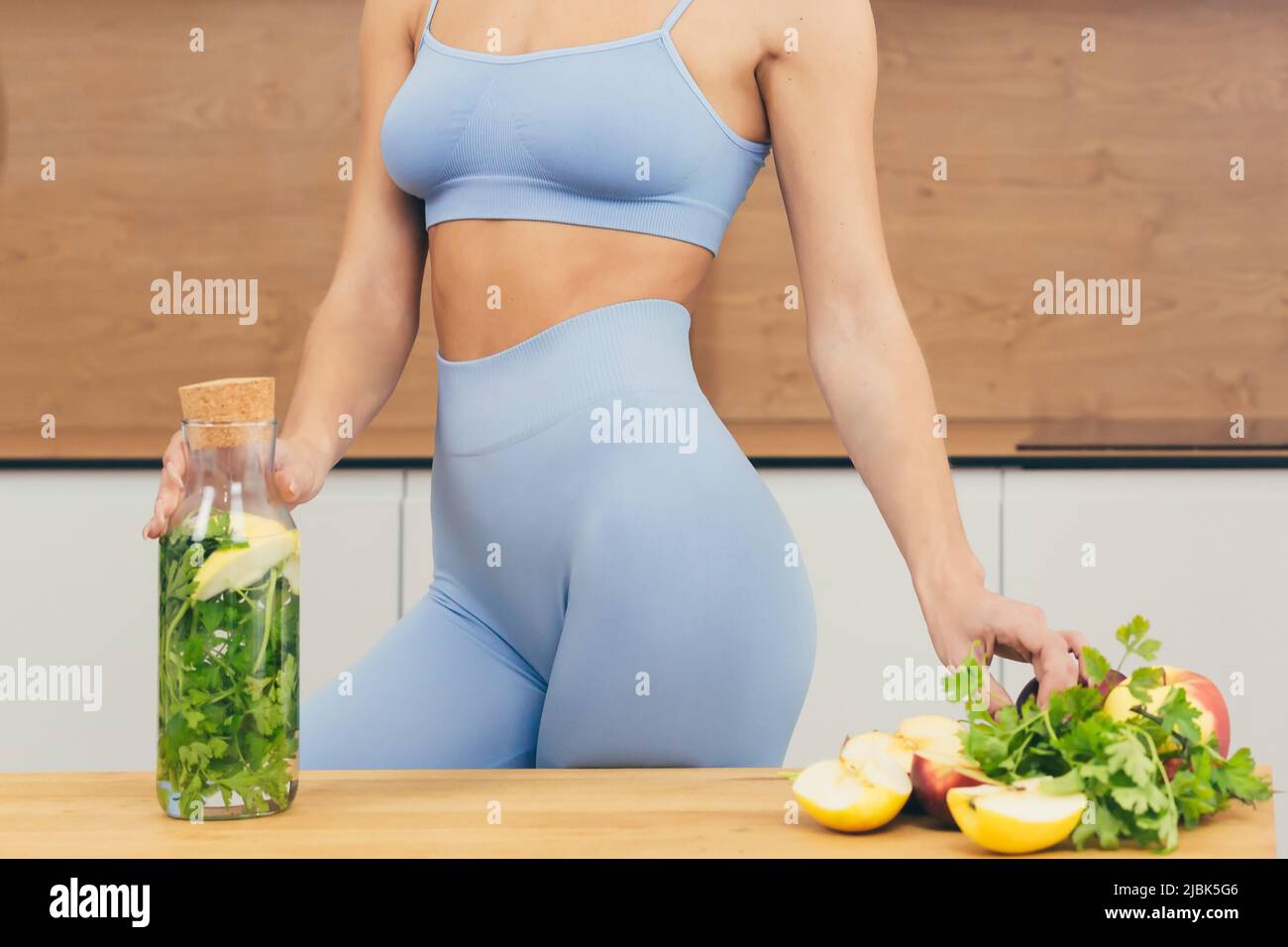 Close up photo body part of young fitness woman standing and holding bottle with fresh juice, detox and fresh vegetables at home in the kitchen Stock Photo