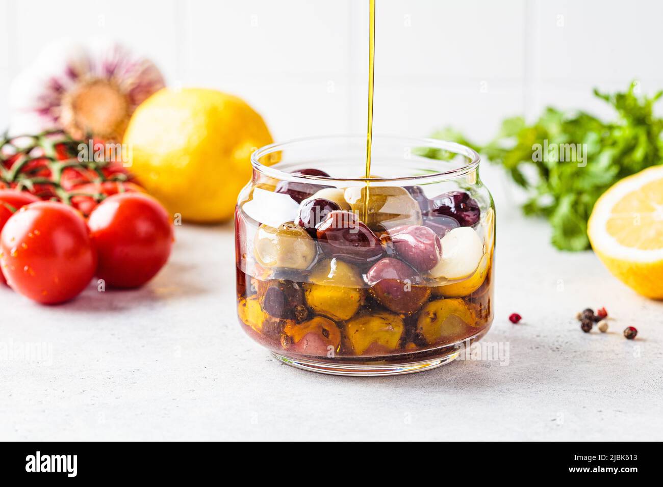 Marinated olives in jar pouring olive oil, white kitchen background