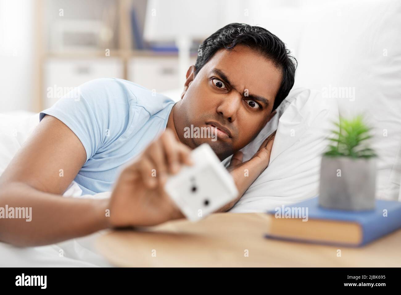 overslept indian man in bed looking at alarm clock Stock Photo