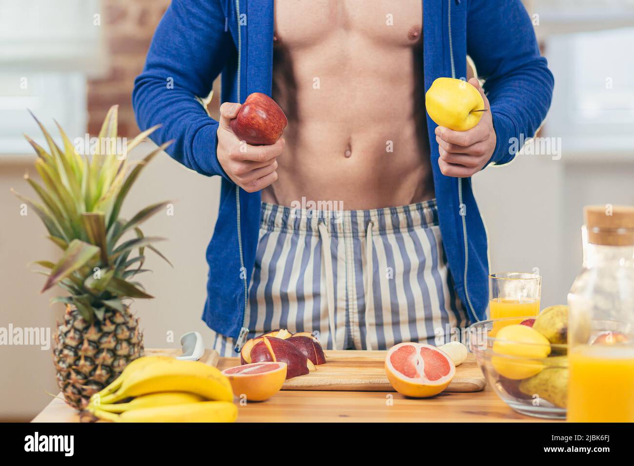 Close up photo, part of body, Male athlete preparing fruit salad and fresh juice at home in the kitchen, showing Stock Photo
