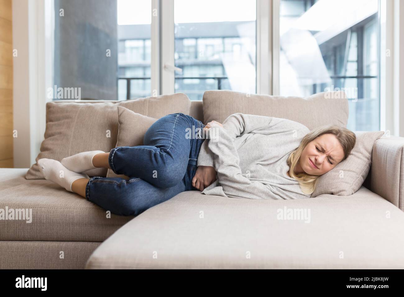 A young woman is lying on the couch at home, holding on to a stomach