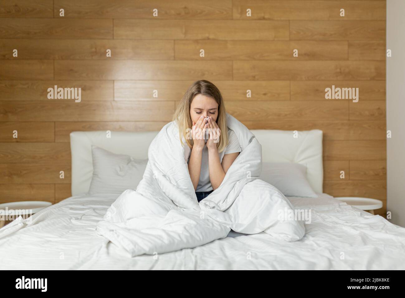 Young woman sitting on the bed at home covered with a blanket, sick