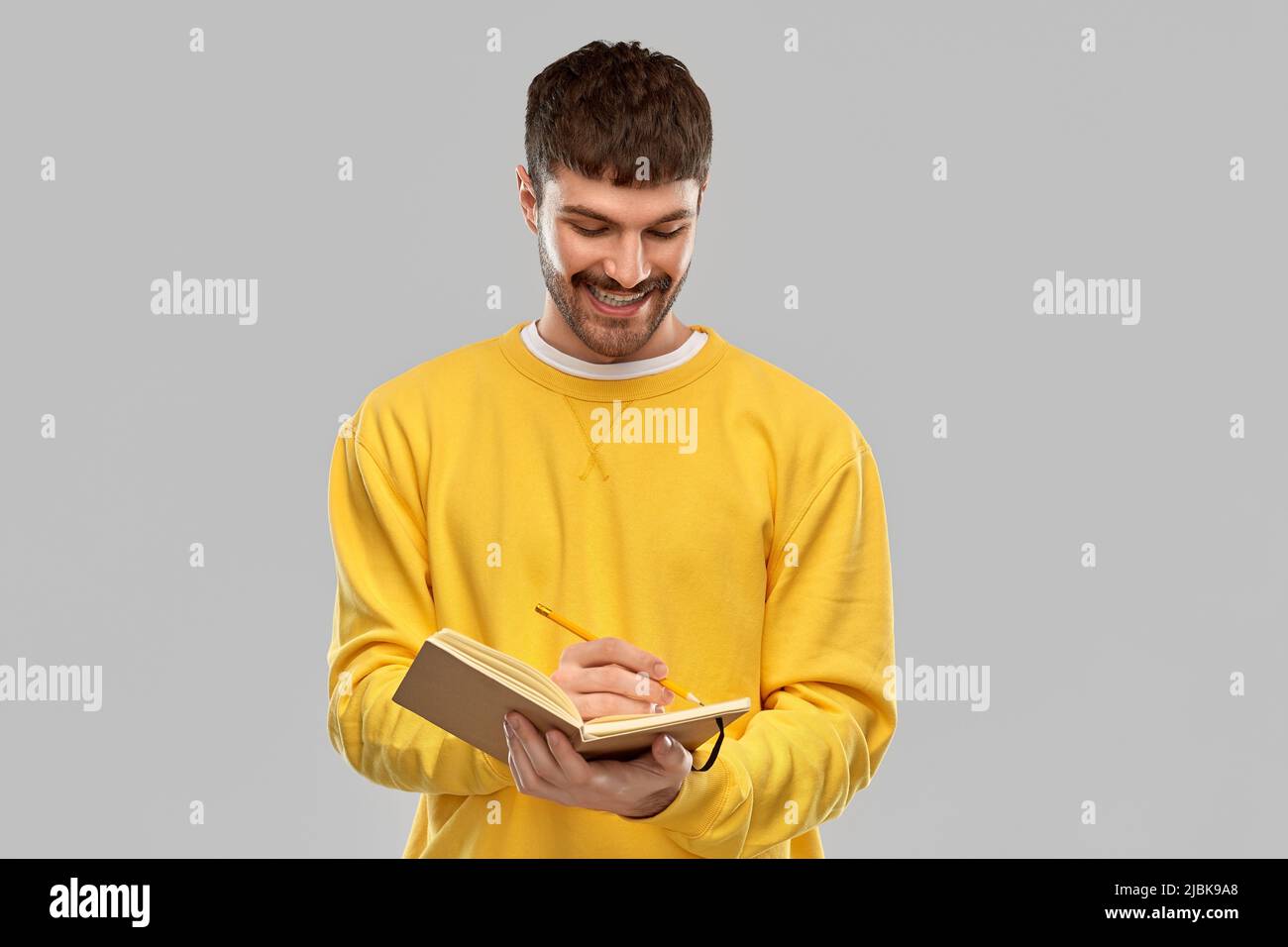 smiling man in yellow sweatshirt writing to diary Stock Photo