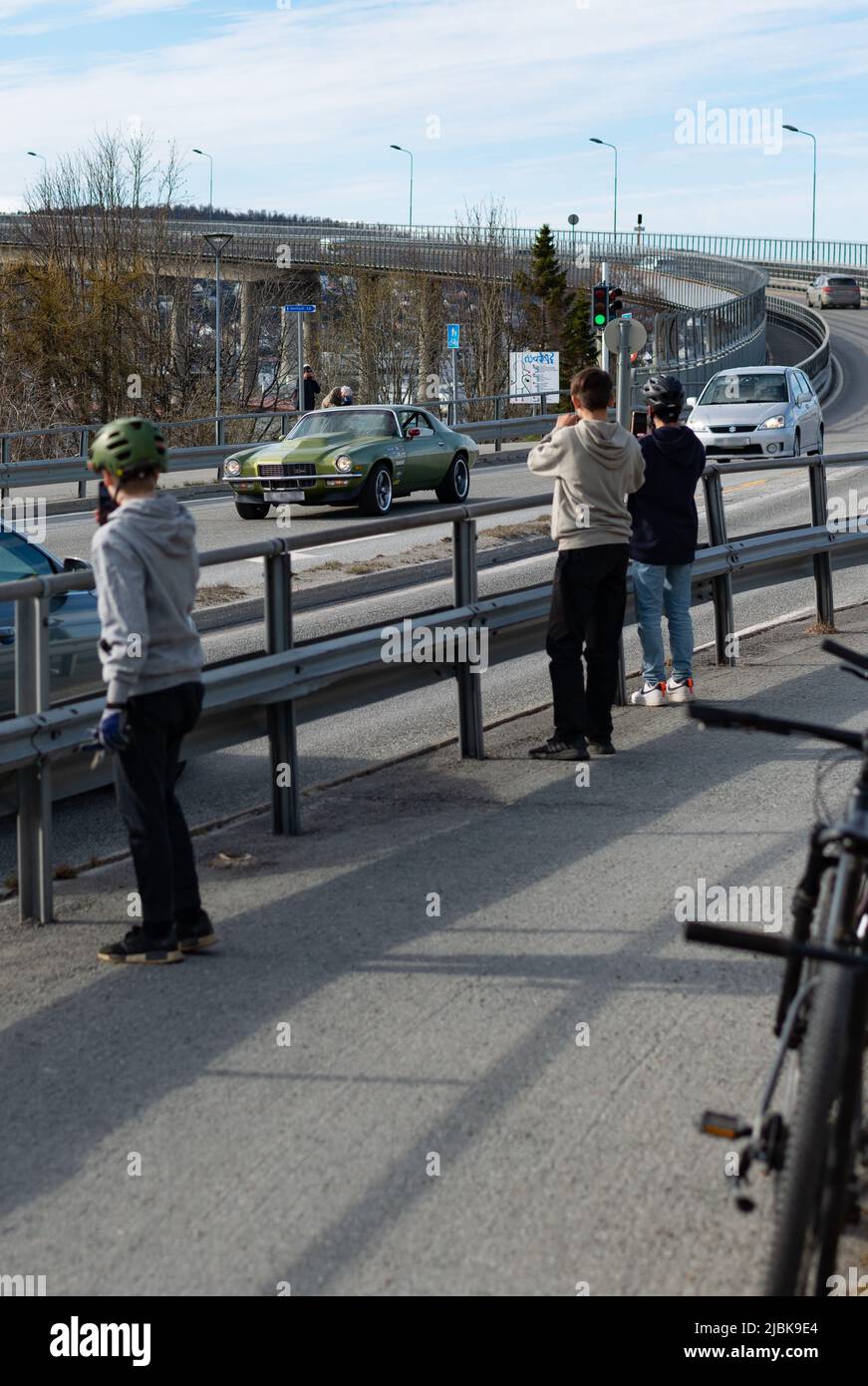 Three boys spotting a veteran chevrolet in Tromsdalen, Tromsø, Norway. They are taking photos with their phones. Their bicycles in the background. Stock Photo