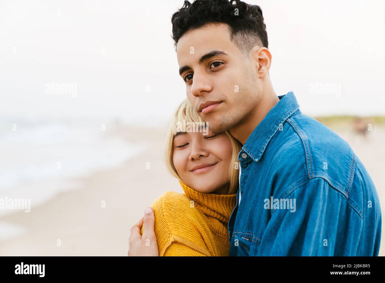 Multiracial young couple hugging while walking on beach Stock Photo