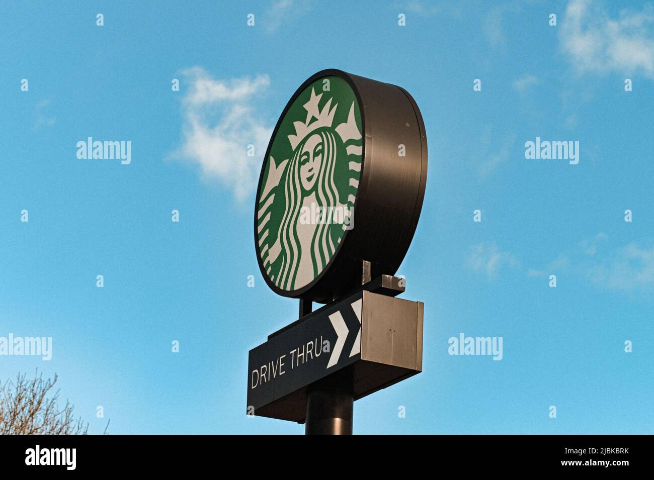 A drive thru Startbucks sign , standing tall with the backdrop of a blue sky with wispy clouds, one person, one cup and one neighborhood at a time Stock Photo