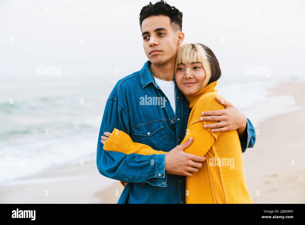 Multiracial young couple hugging while walking on beach Stock Photo