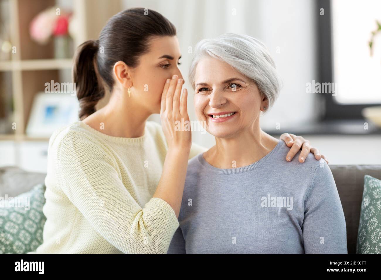 adult daughter whispering secret to senior mother Stock Photo