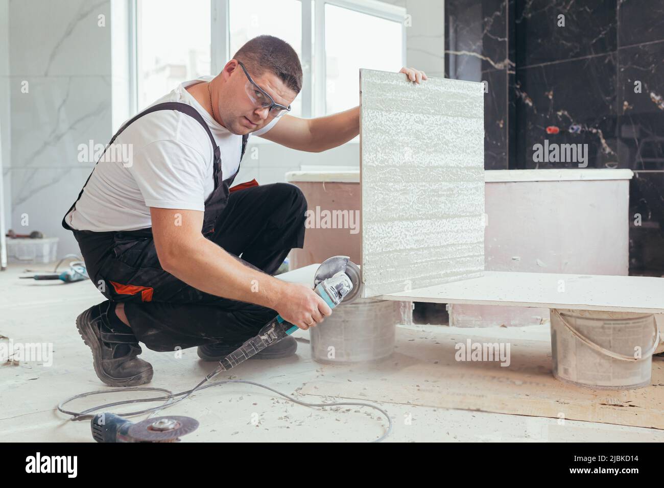 male worker cuts a large ceramic tile with an electric saw with a hand