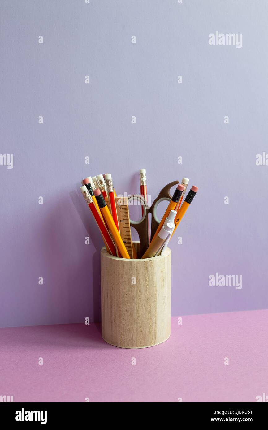 Pencils and various stationery in wooden holder on purple desk. purple wall background Stock Photo