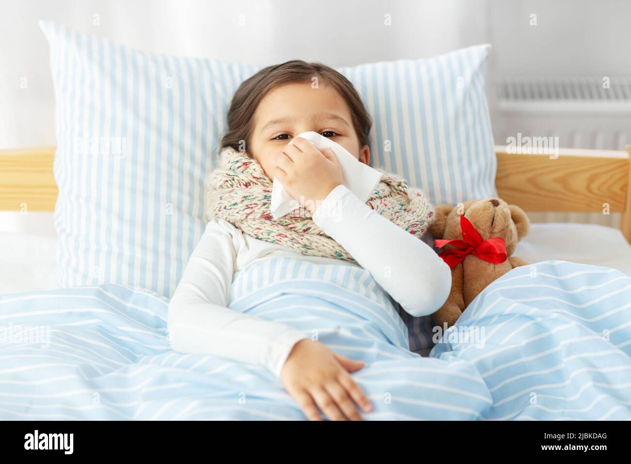 sick girl lying in bed and blowing nose at home Stock Photo