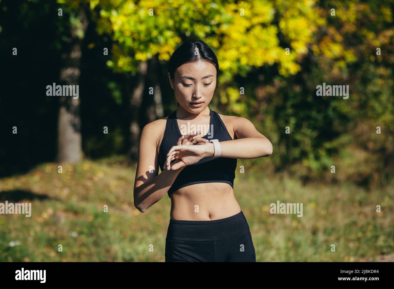 Sporty asian woman looking smart watch at modern track runner using use smartwatch fitness bracelet Portrait fitness female athlete checking result jo Stock Photo