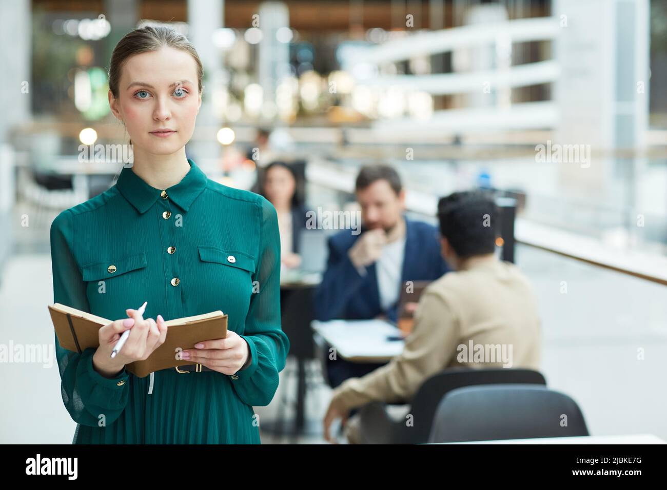 Waist up portrait of young businesswoman holding planner and looking at camera in office building interior, copy space Stock Photo