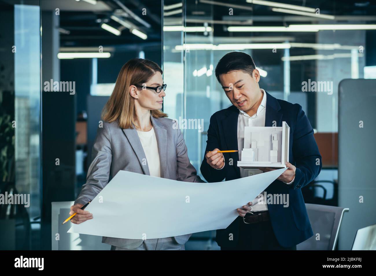 Group young creative engineers Developers discussing new project standing in office reading a blueprint. Team architect designer conversations Asian m Stock Photo