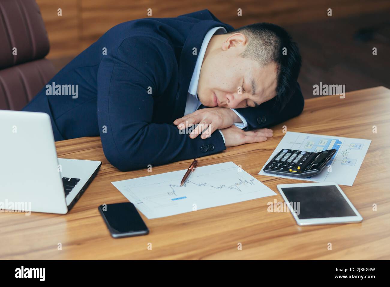 Tired young asian man businessman, worker. Lawyer fell asleep on his hands on the desk at work in the office Stock Photo