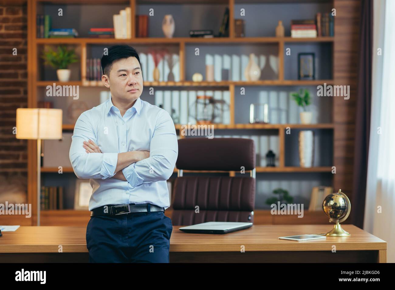 Portrait of a pensive businessman, a man with arms crossed in a classroom office working, looking out the reverse window, Asian thinks Stock Photo