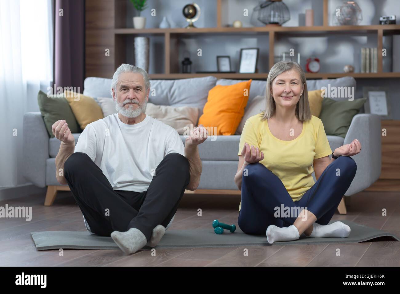 senior man and woman in the house doing yoga, family on a mat, in the lotus position looking at the camera together, morning exercise and fitness Stock Photo