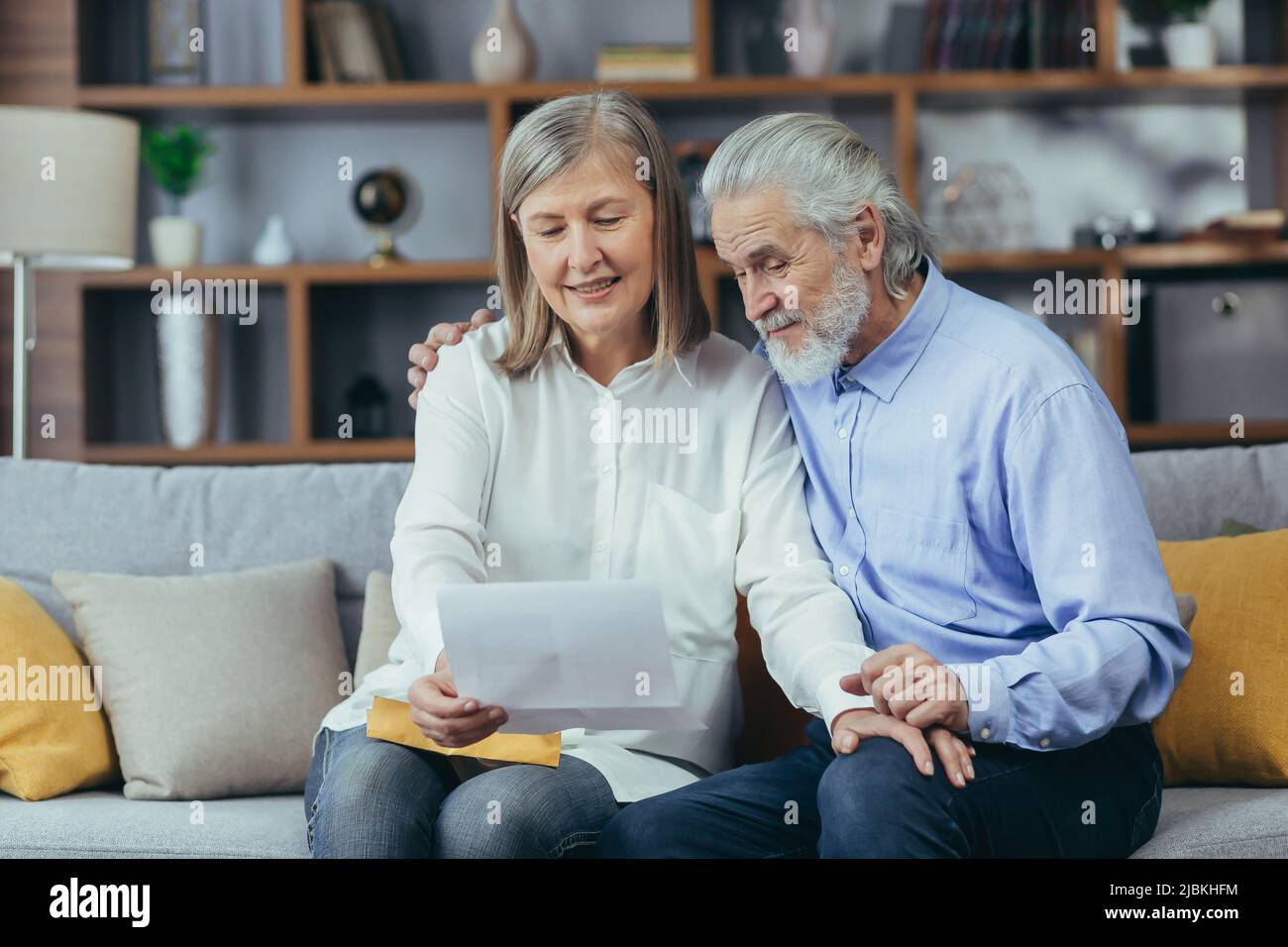 Happy Senior Retired Couple Sitting On Sofa At Home Reading Letter Happy And Smiling Stock