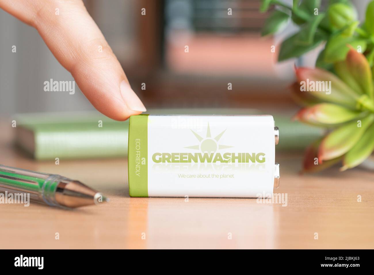Greenwashing concept, woman hold a finger over a battery with the text: greenwashing, we care about the planet Stock Photo
