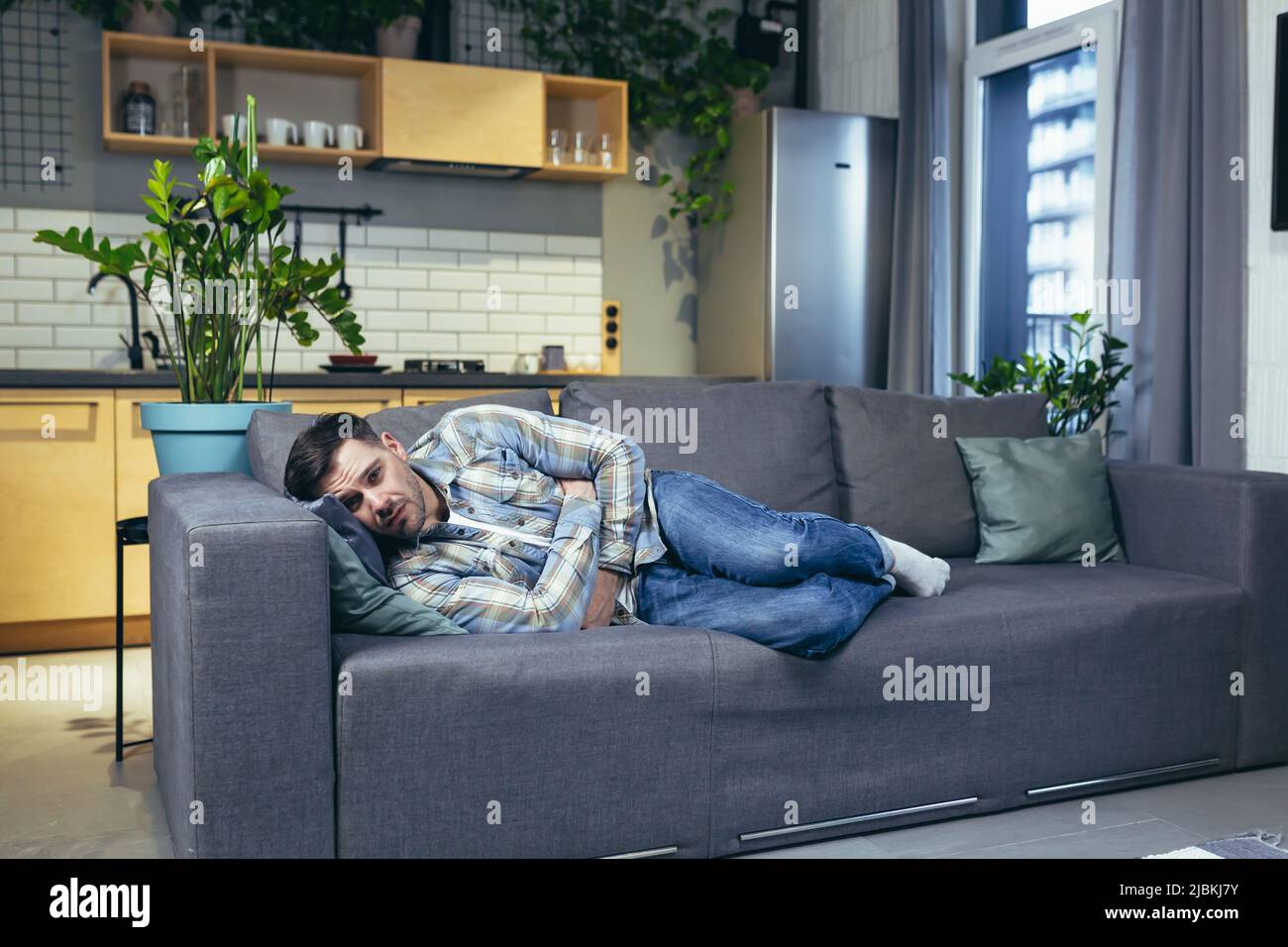 A young man is sleeping and lying on the couch at home. Tired, feeling bad, sick Stock Photo
