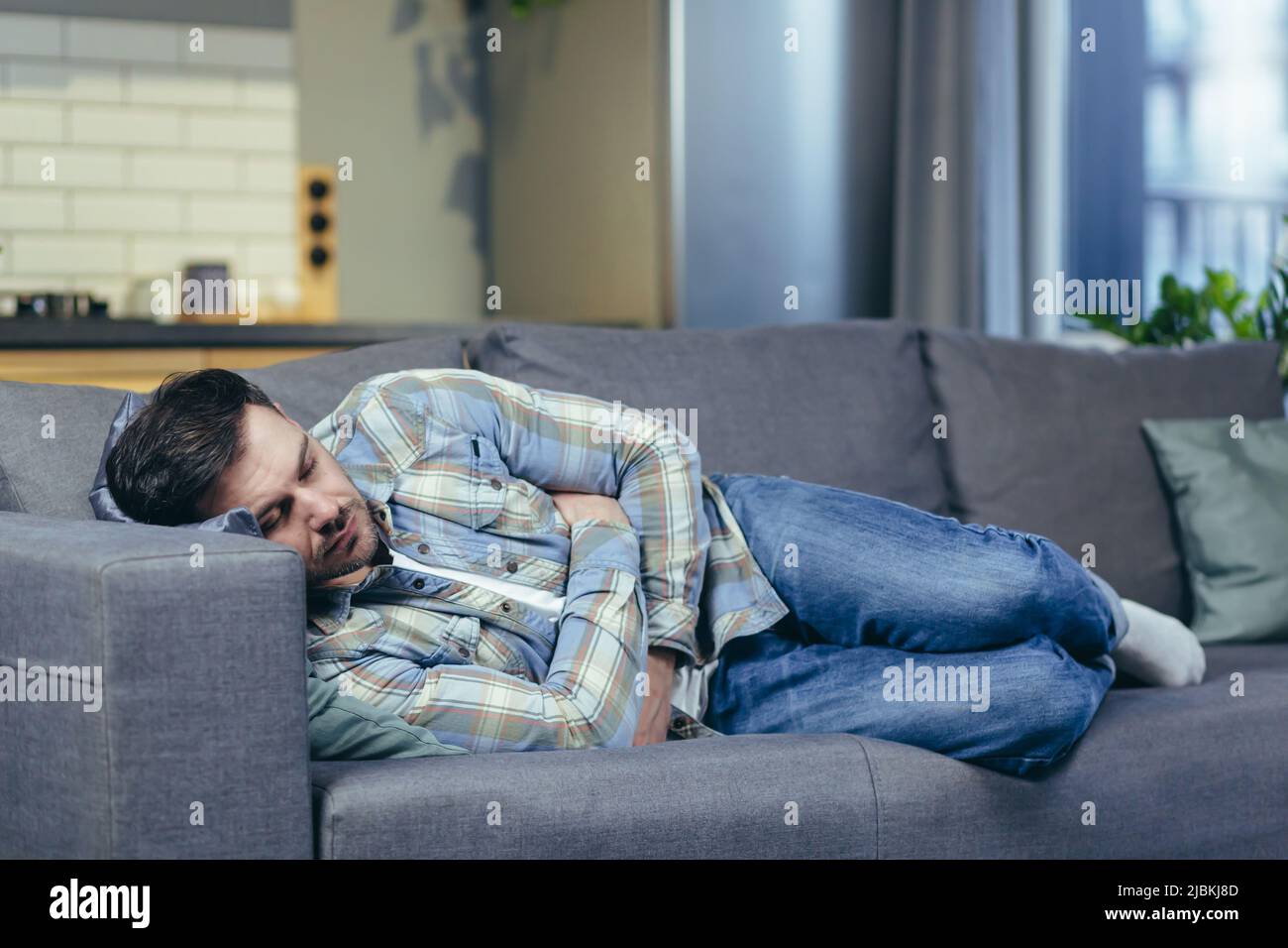 A young man is sleeping and lying on the couch at home. Tired, feeling