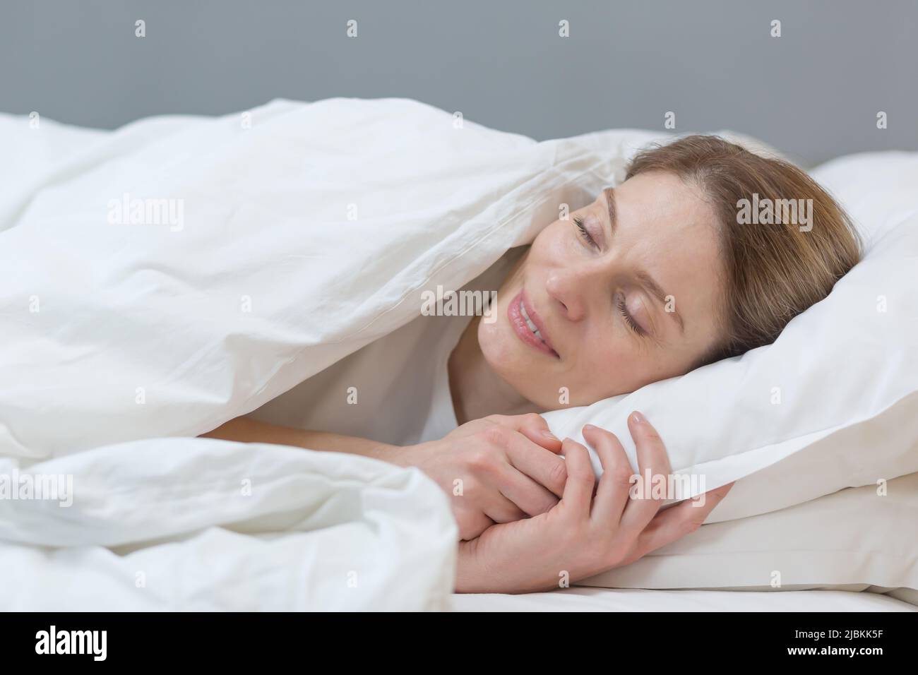 Closeup photo of a woman sleeping under a blanket smiling in a dream