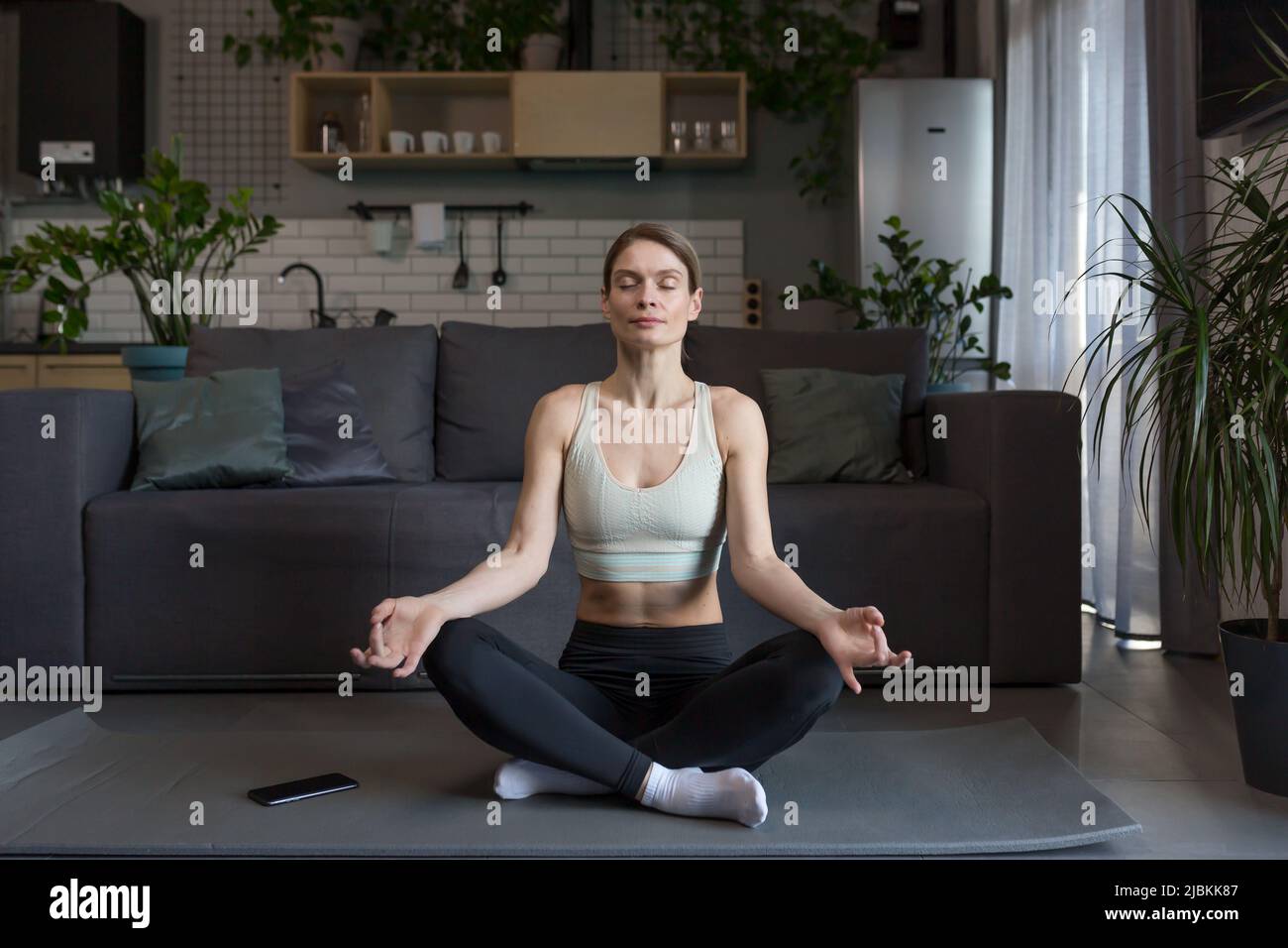 Woman at home sitting on the floor in the lotus position, meditating ...