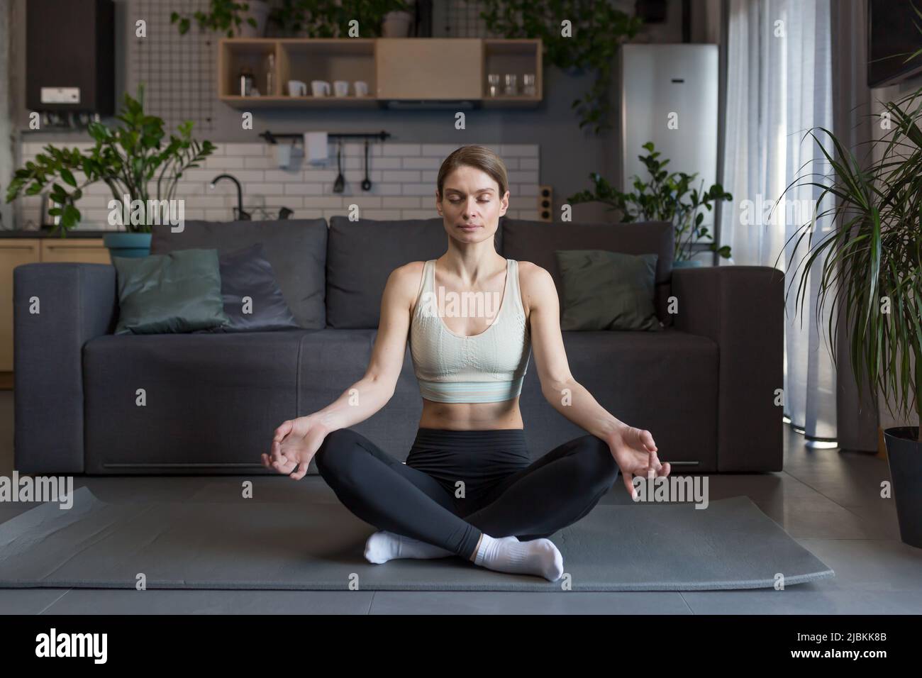 Woman at home sitting on the floor in the lotus position, meditating ...