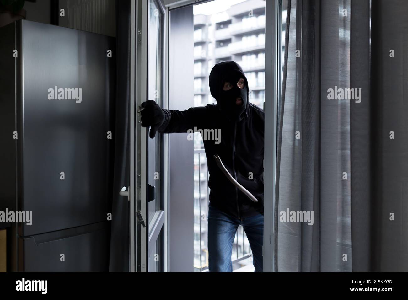 A male thief in a black mask, enters the apartment for robbery, the