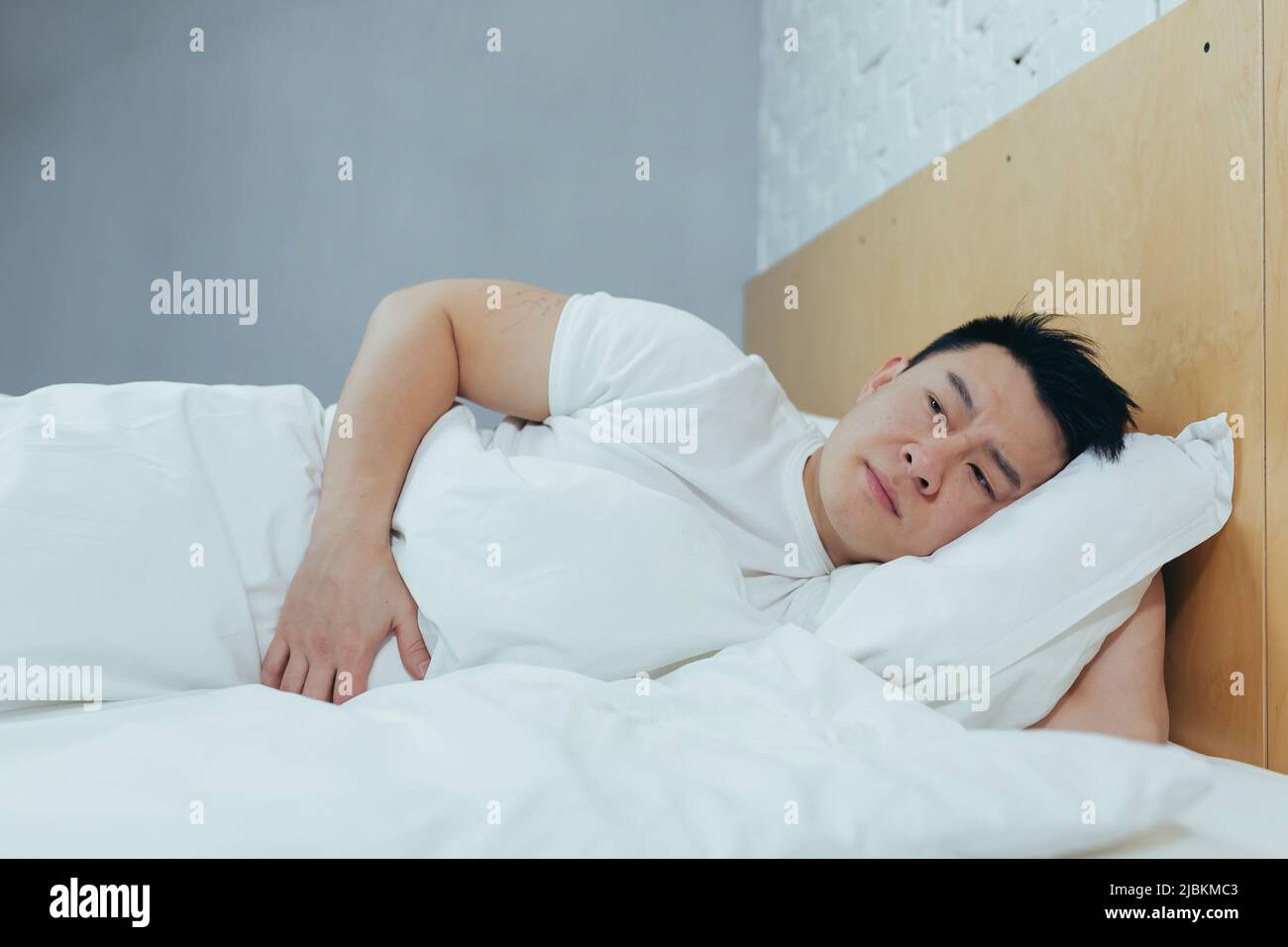 A man lying in bed has abdominal pain, an Asian sleeps in bed under a