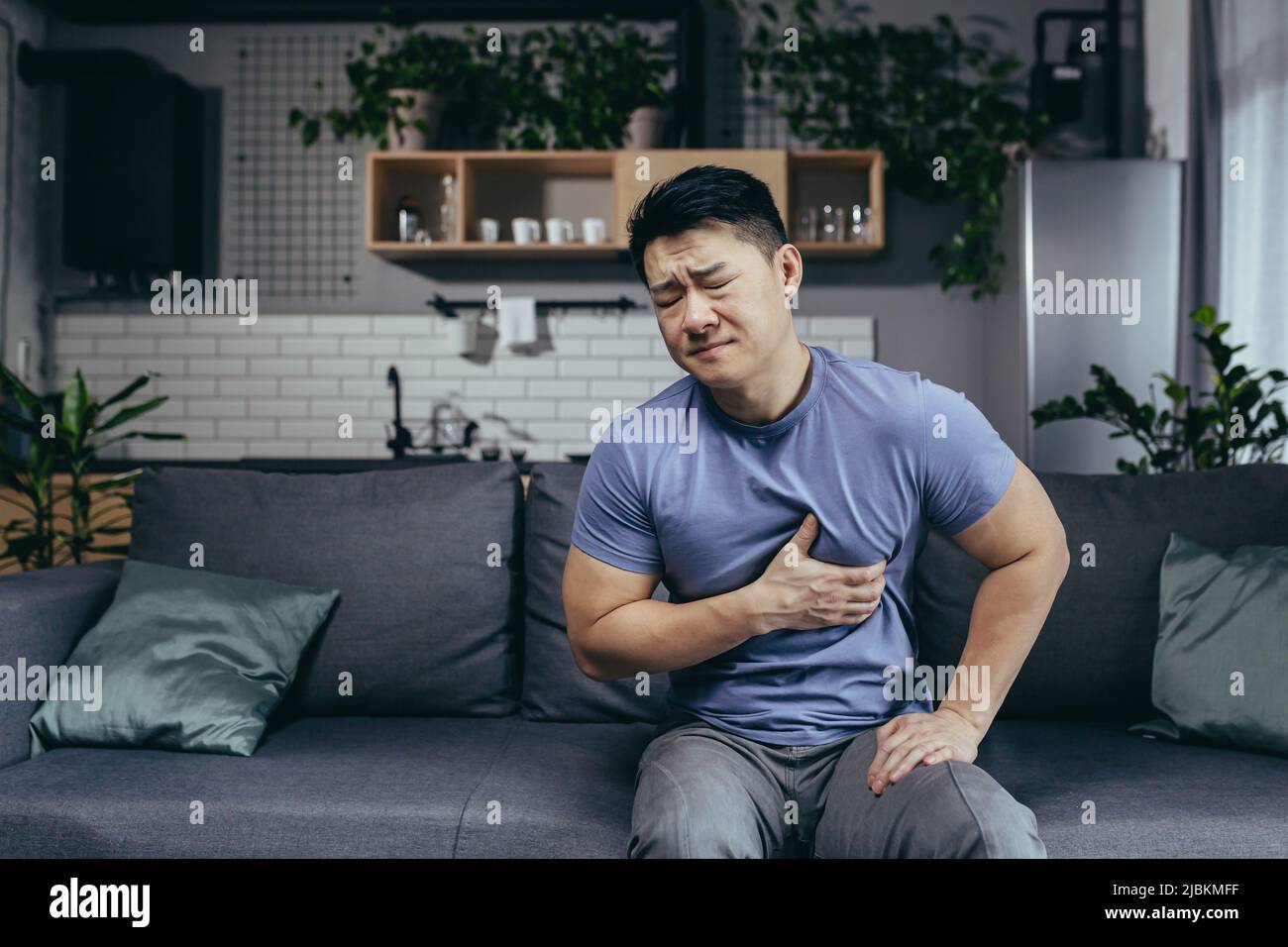 A man at home sitting on a sofa in the living room, an Asian patient has severe chest pain, heart disease Stock Photo