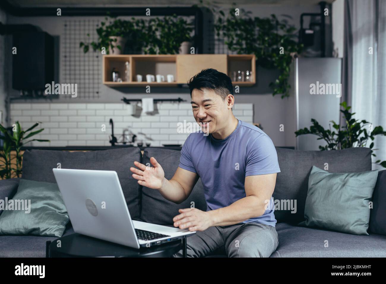 Asian at home talking on video, uses laptop, looks at the screen, man