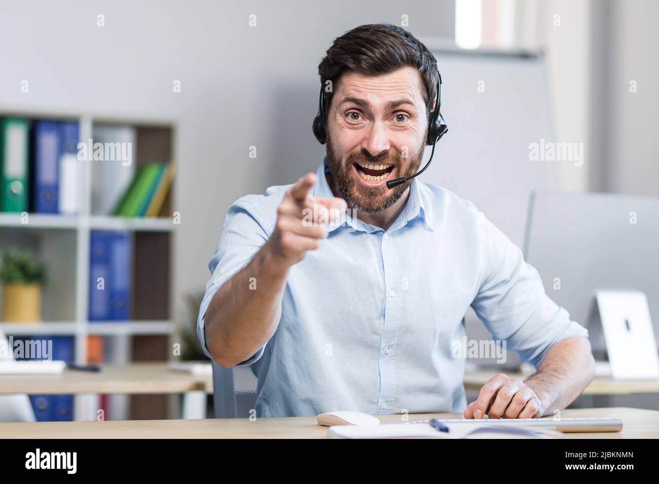 A young man, a consultant, an office worker, a manager talking on a video call in headphones, waving his arms, explaining something. Sitting at a comp Stock Photo