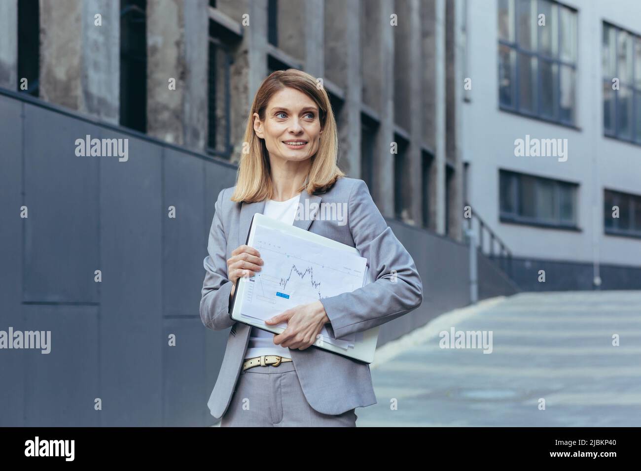 Happy and successful business woman with laptop and documents outside ...
