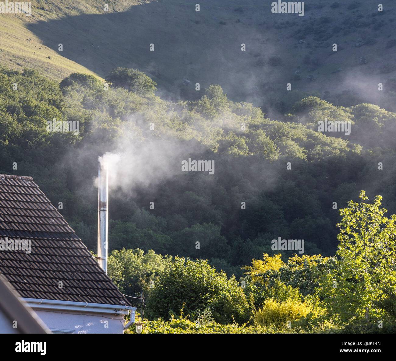 Smoking woodburner chimney on house in village, Wales, UK Stock Photo