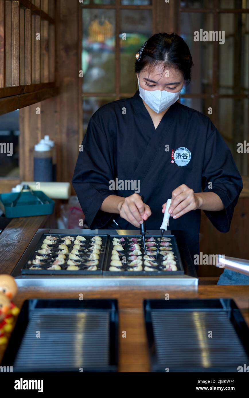 Female chef in a Japanese restaurant cooking traditional Japanese Takoyaki dumplings Stock Photo