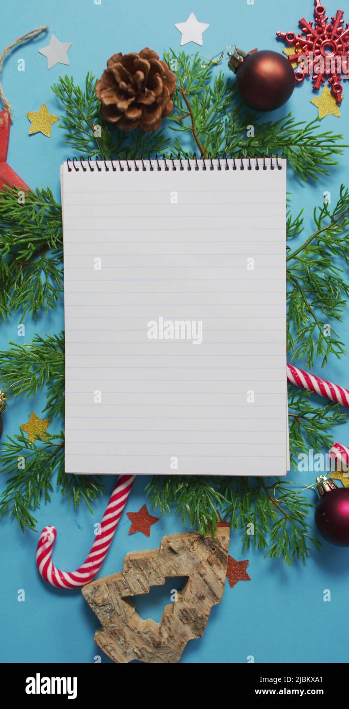 Vertical overhead shot of a notebook surrounded by Christmas decorations on a blue background Stock Photo